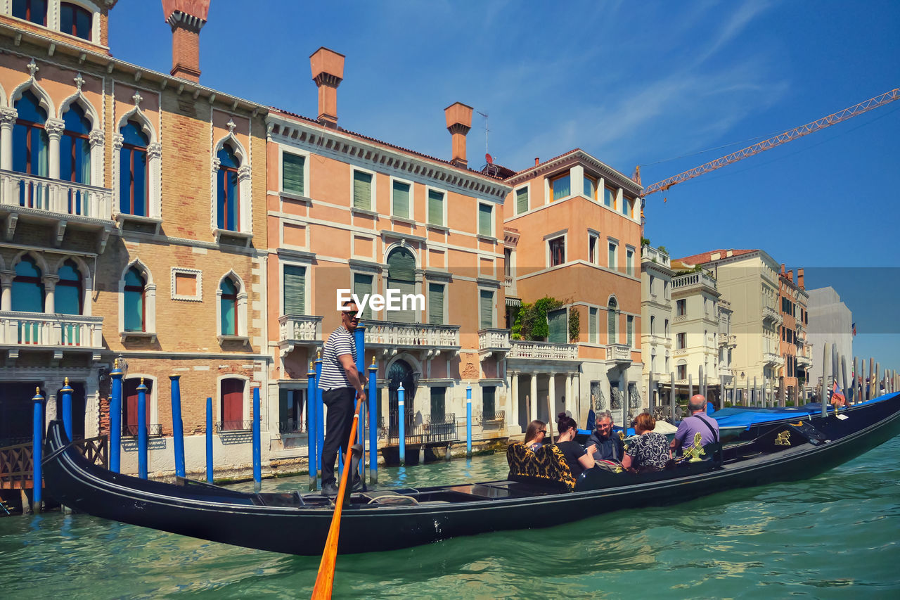 gondola, nautical vessel, water, transportation, canal, architecture, mode of transportation, travel, travel destinations, gondolier, building exterior, boat, tourism, vehicle, nature, built structure, watercraft, city, trip, vacation, holiday, tourist, group of people, waterway, sky, romance, men, adult, love, outdoors, day, blue, women, journey, multi colored, sunlight, sea, rowing, building, crowd, lifestyles, bridge, boating, lagoon, craft, town