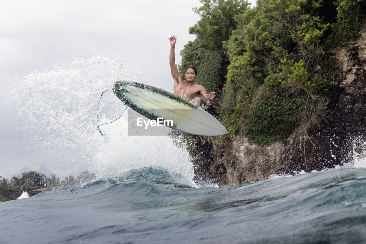 Young male surfer jumping over sea