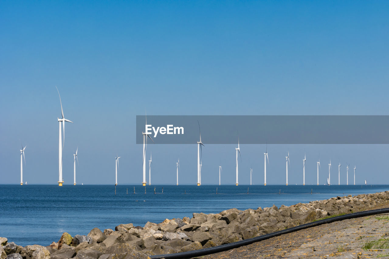 Wind turbines by sea against clear blue sky,