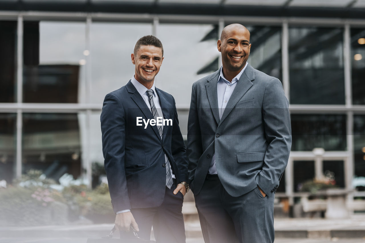 Portrait of smiling male corporate professionals wearing suit while standing in front of building