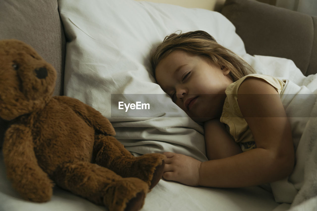 Portrait of cute little girl sleeping in bed with toy bear