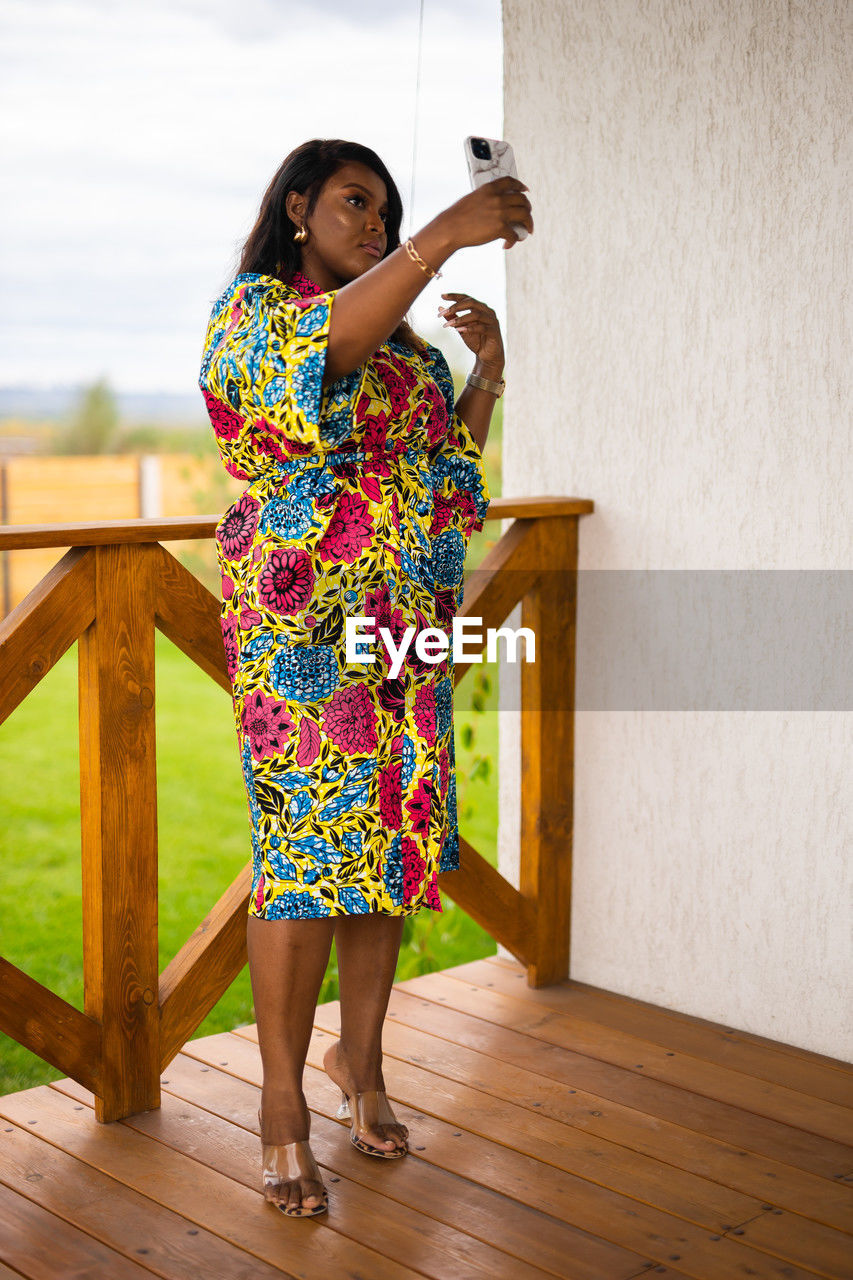 one person, women, standing, spring, full length, adult, clothing, dress, lifestyles, holding, fashion, female, architecture, yellow, leisure activity, wood, young adult, pattern, portrait, casual clothing, nature, floral pattern, looking, hairstyle, happiness, smiling, photo shoot, emotion, day, outdoors, person, child, relaxation, water, childhood