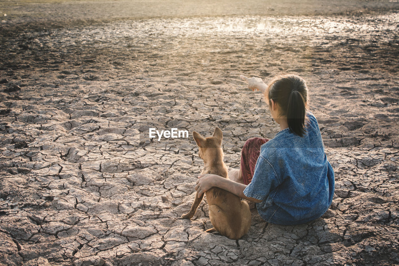 High angle view of girl with dog sitting on field during drought