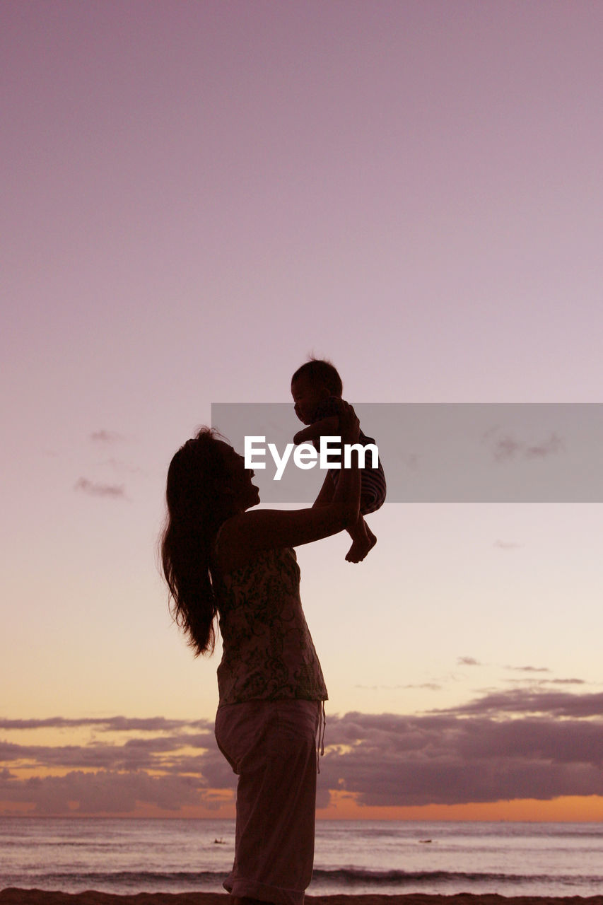 Side view of mother with baby boy on beach during sunset