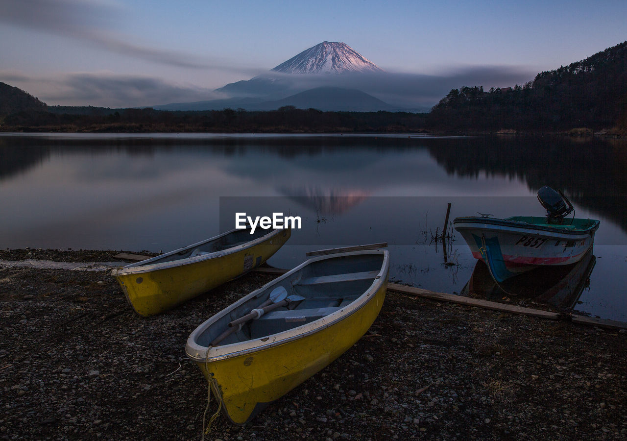 BOATS MOORED ON LAKE SHORE AGAINST SKY