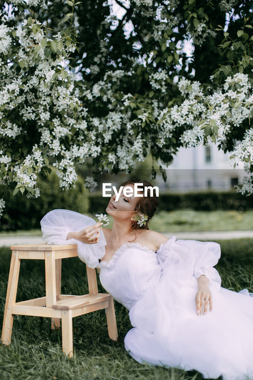 A beautiful delicate woman bride in a wedding dress walks alone in a blooming spring outdoor park