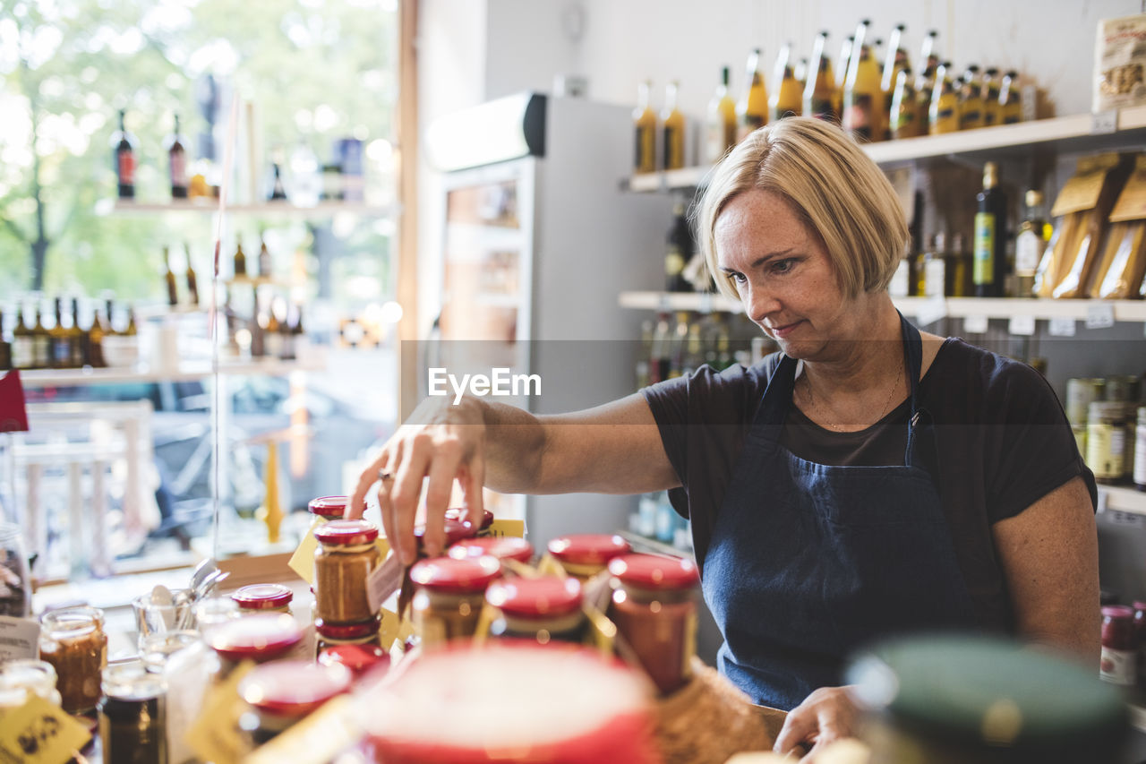 Mature female employee arranging jars in deli