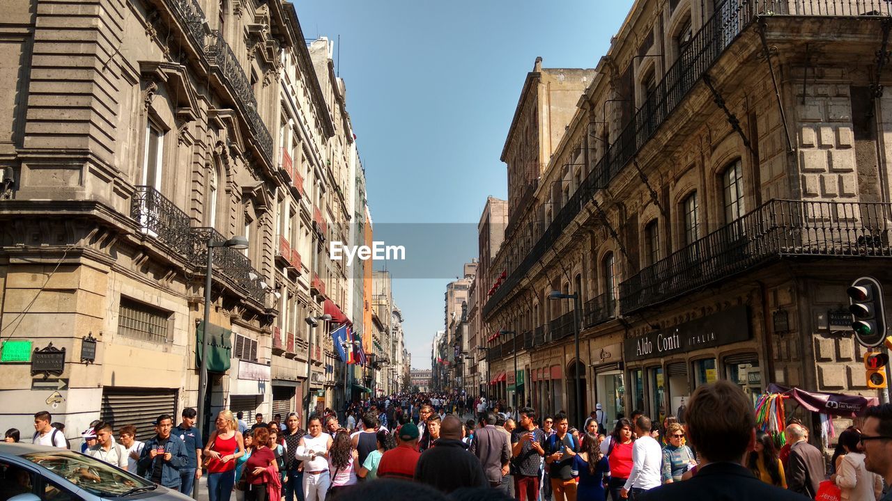 PEOPLE ON STREET AMIDST BUILDINGS IN CITY AGAINST SKY