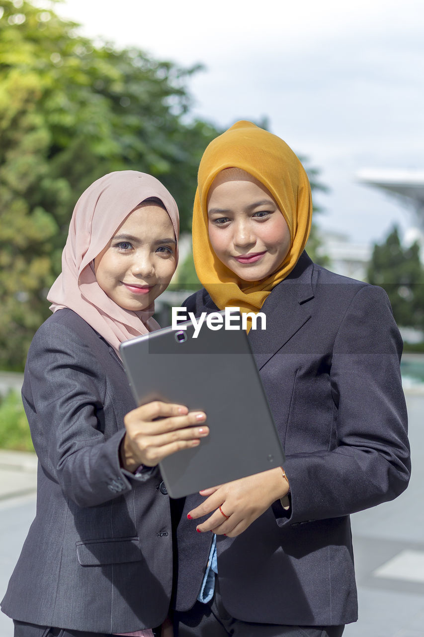 Portrait of businesswomen taking selfie through digital tablet with colleague on street
