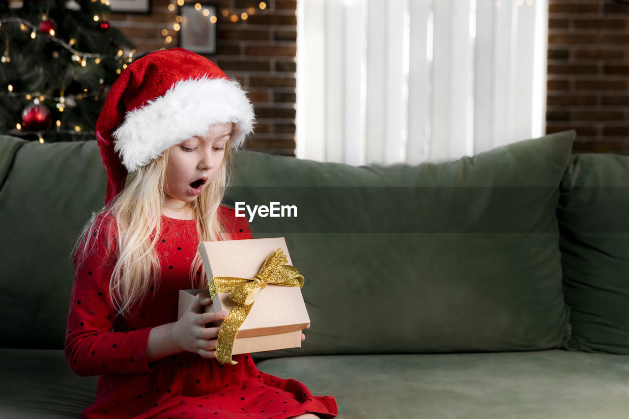 Small little shocked girl in red dress holds christmas or new year gift box present