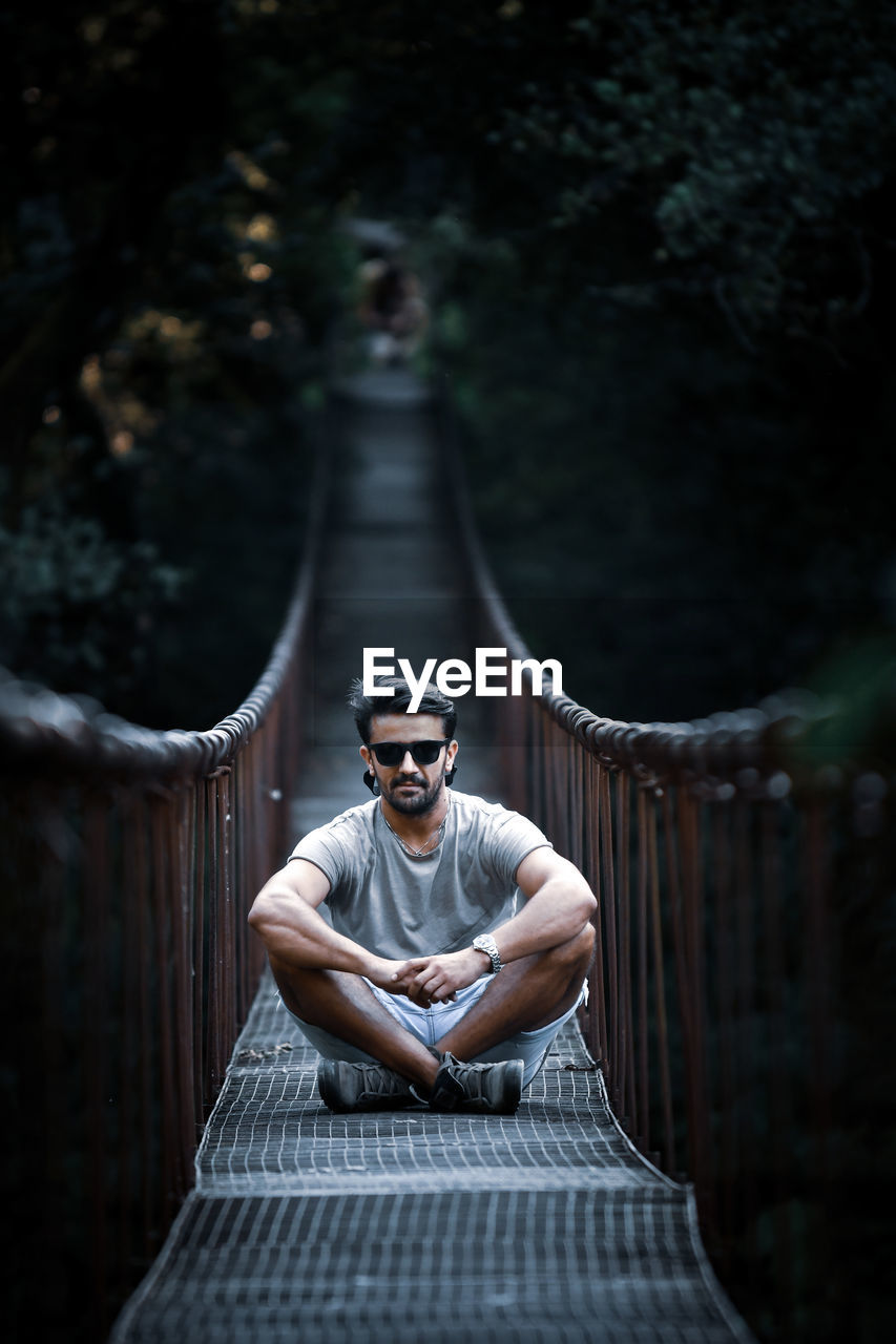 Portrait of man in sunglasses sitting on footbridge