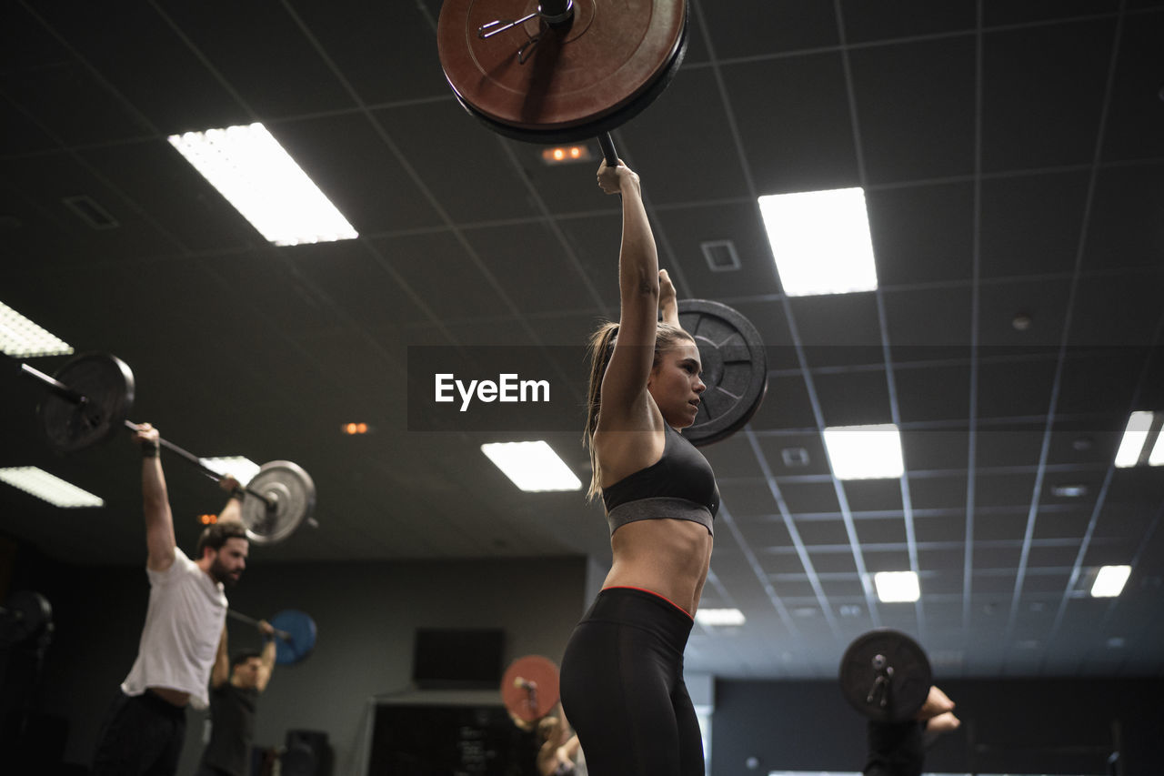 Women and men exercising with barbell while standing in gym