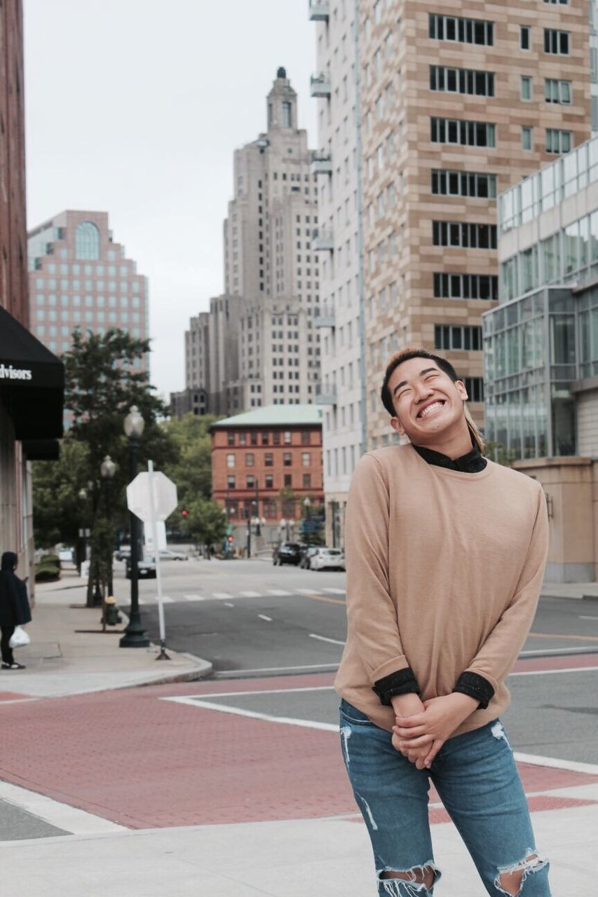 Cheerful young man standing on sidewalk in city