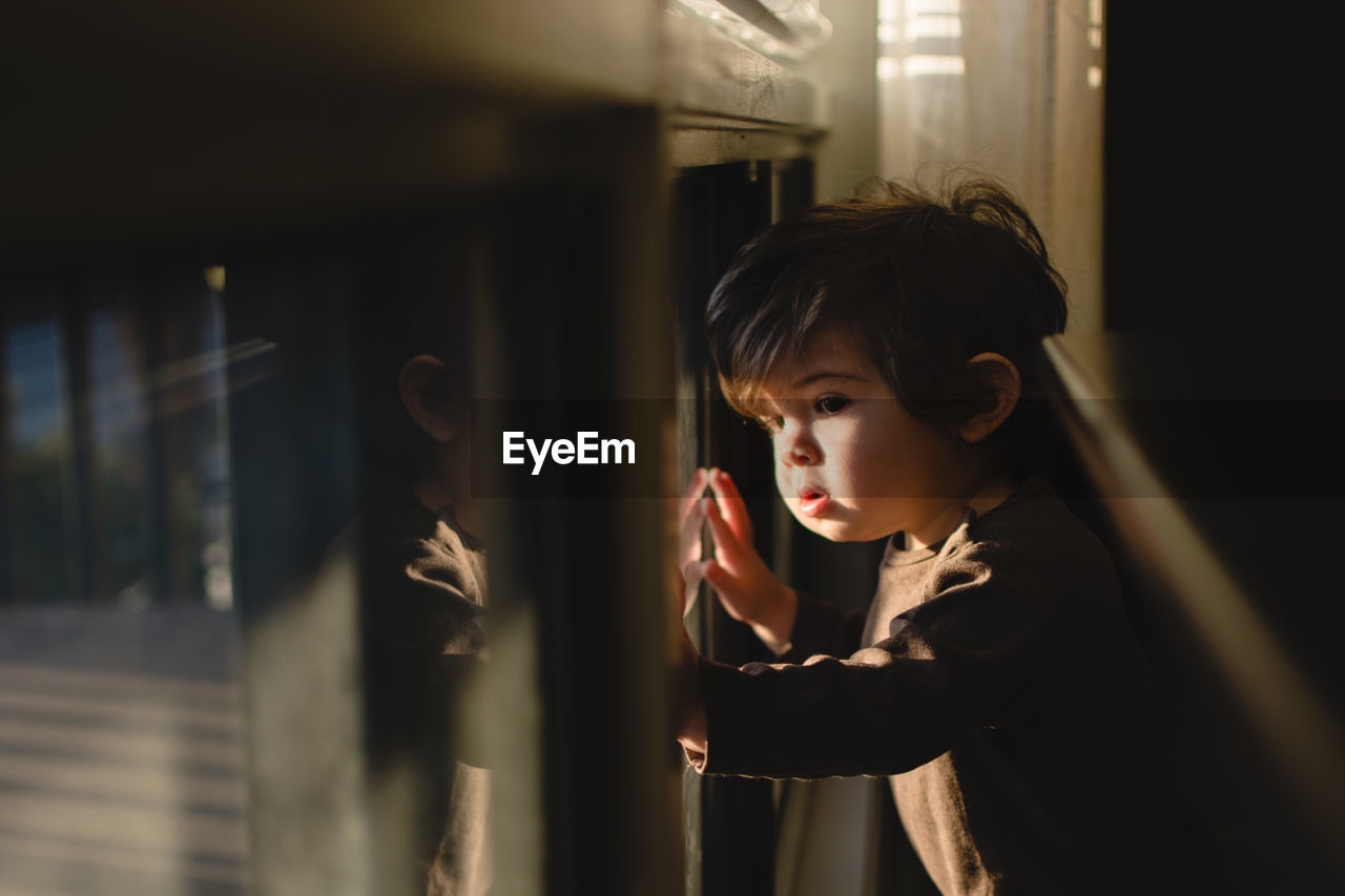 Close-up portrait of young boy looking through window