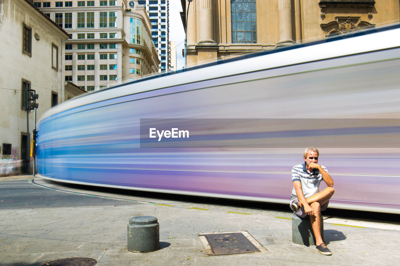 Full length of woman sitting by blurred motion of train in city