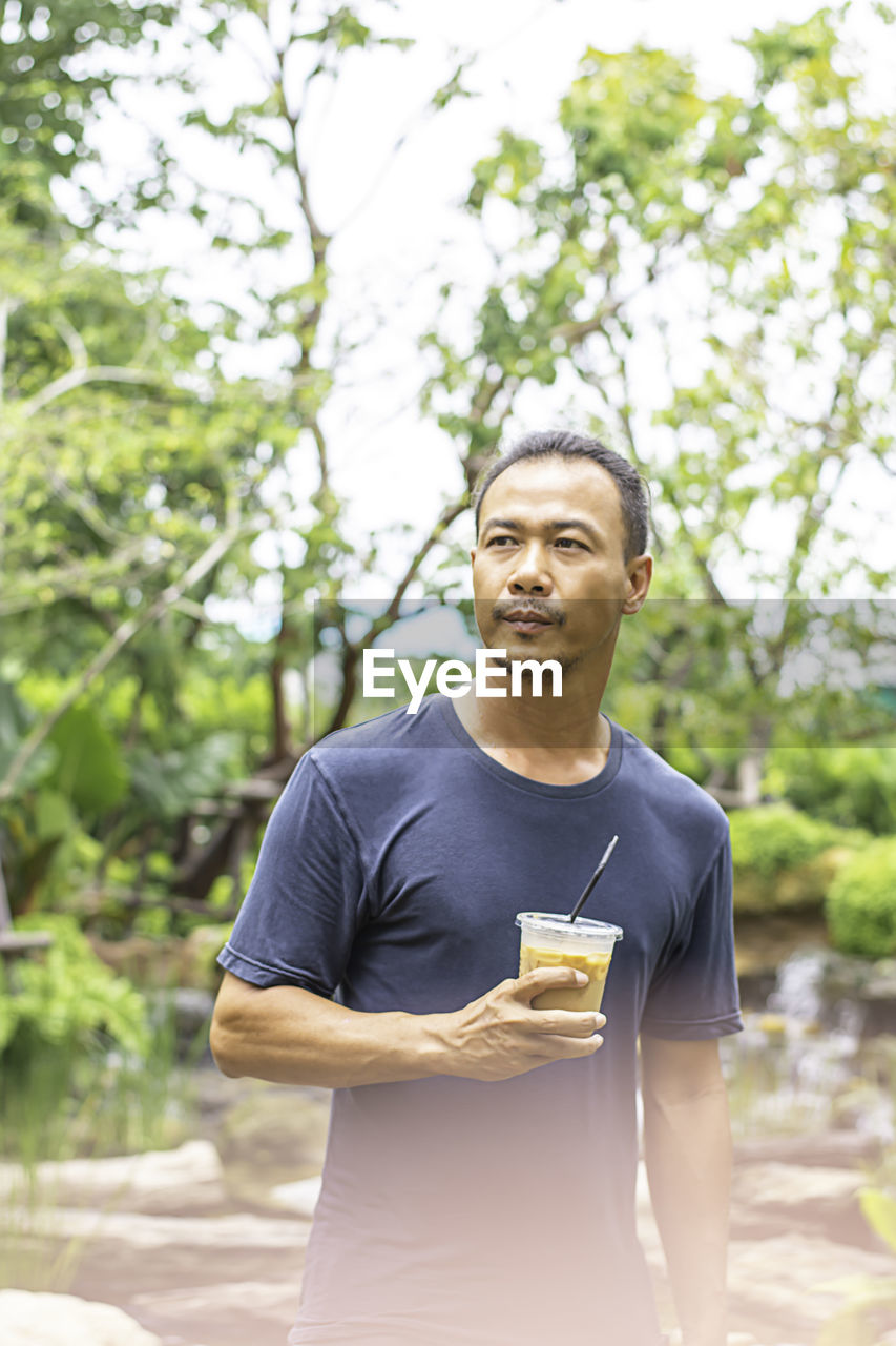 Man holding coffee while standing against trees