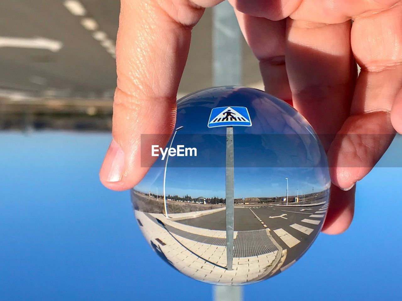Cropped hand holding crystal ball with reflection against road sign