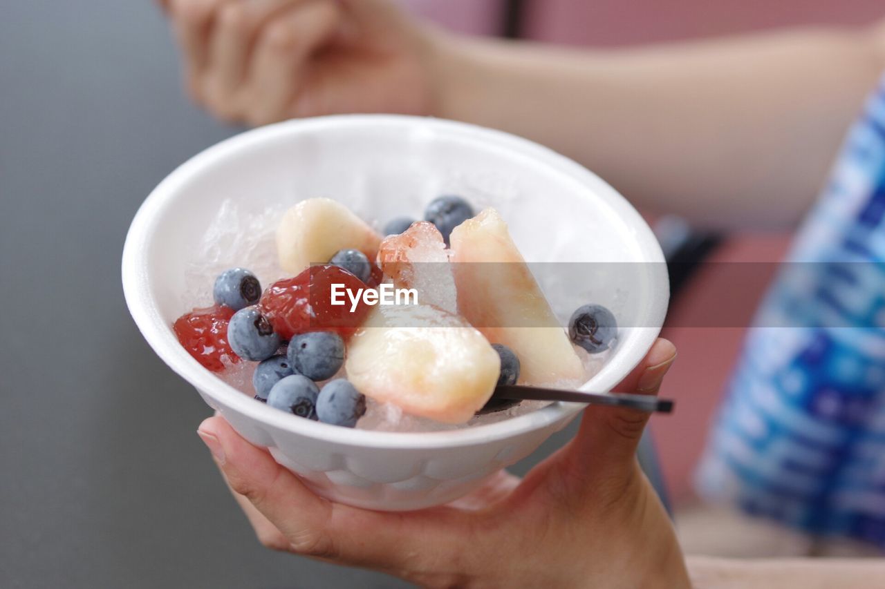 Cropped person holding fruit bowl with ice and spoon