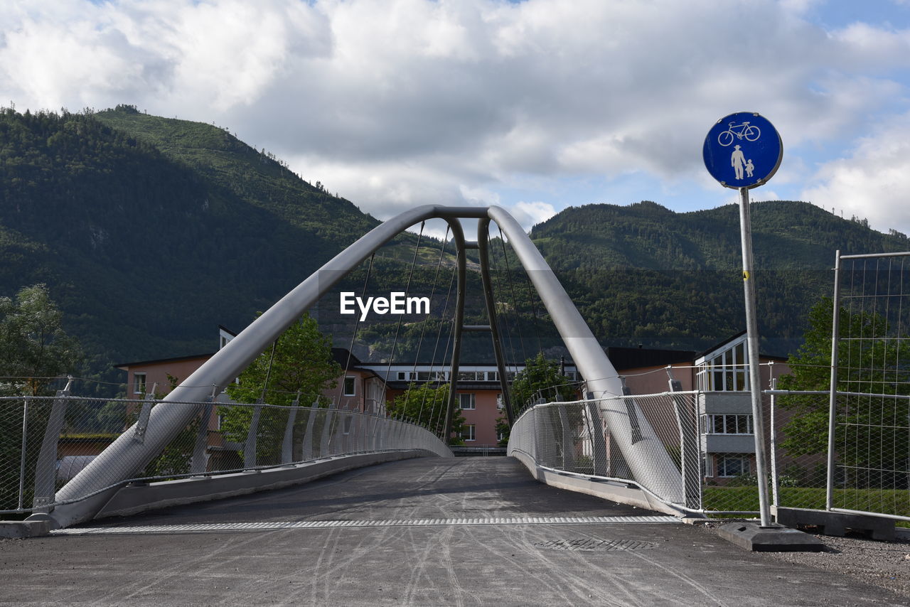 ROAD SIGN ON BRIDGE AGAINST CLOUDY SKY