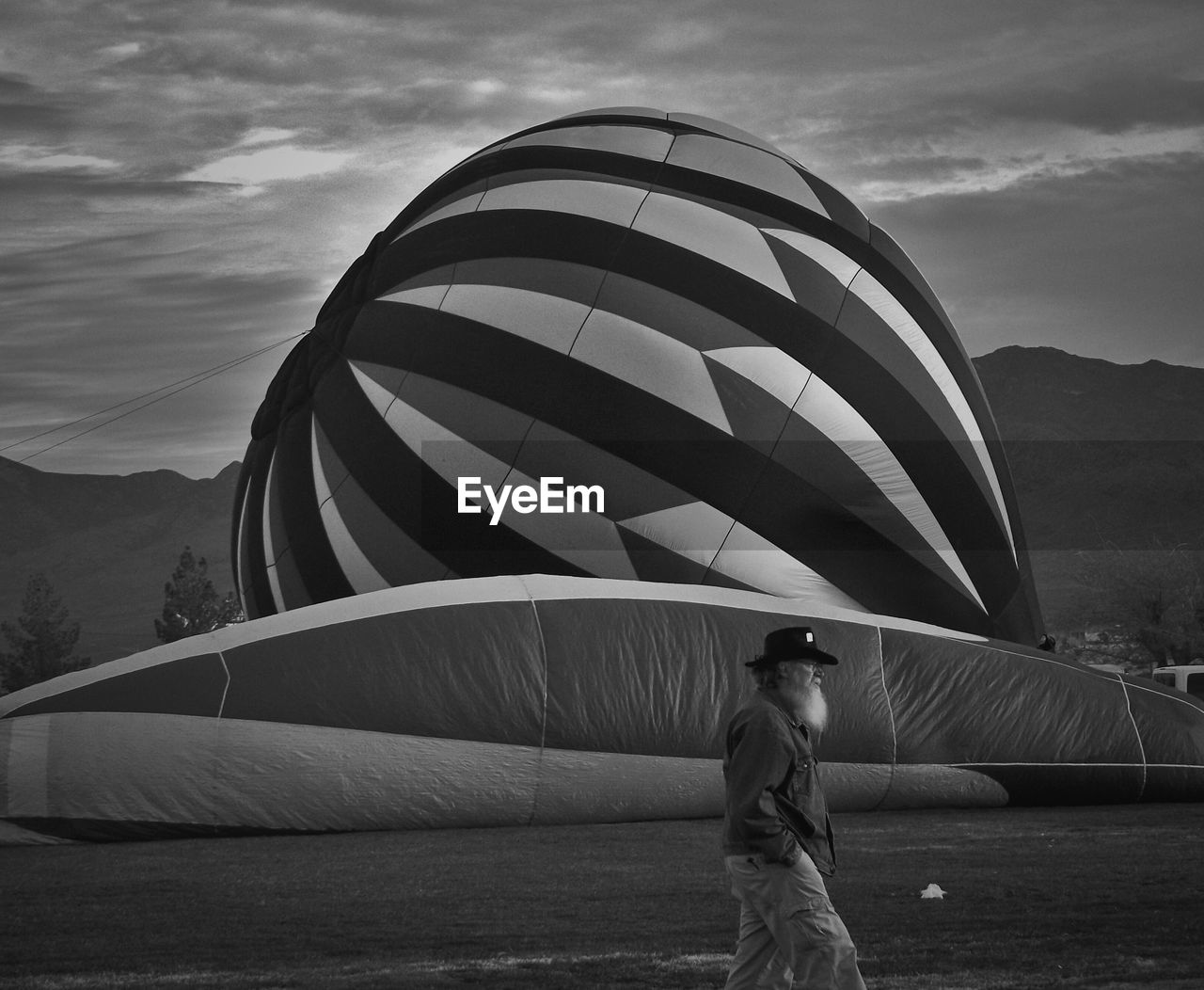 Side view of mature man with hands in pockets walking by hot air balloon on field