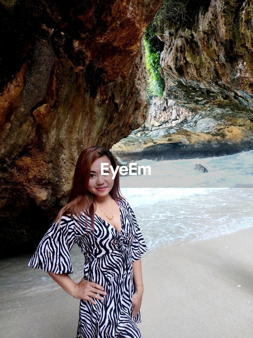 PORTRAIT OF YOUNG WOMAN STANDING ON ROCK AGAINST WATER