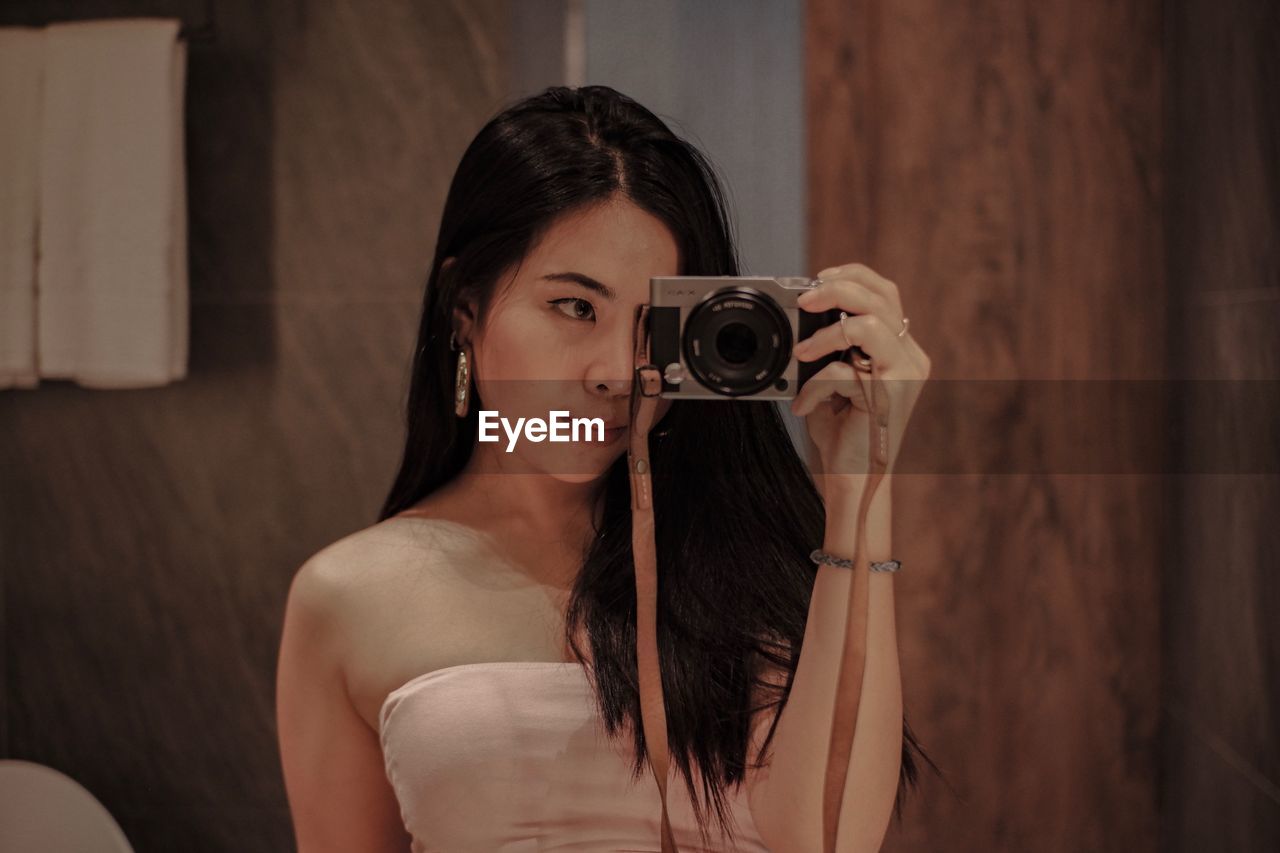 PORTRAIT OF BEAUTIFUL WOMAN HOLDING CAMERA IN MIRROR