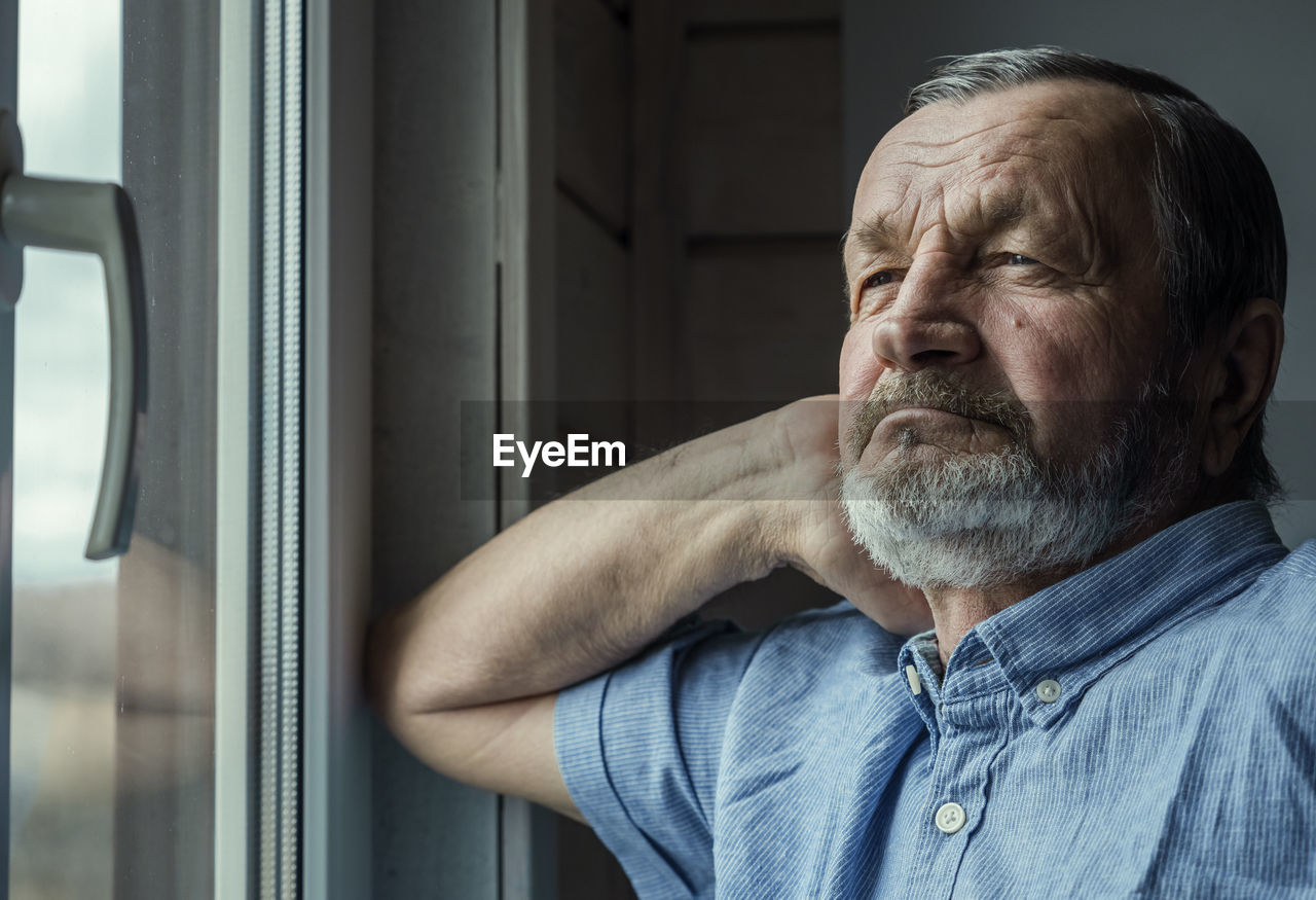 Elderly man at the window at home in his room. covid lockdown concept