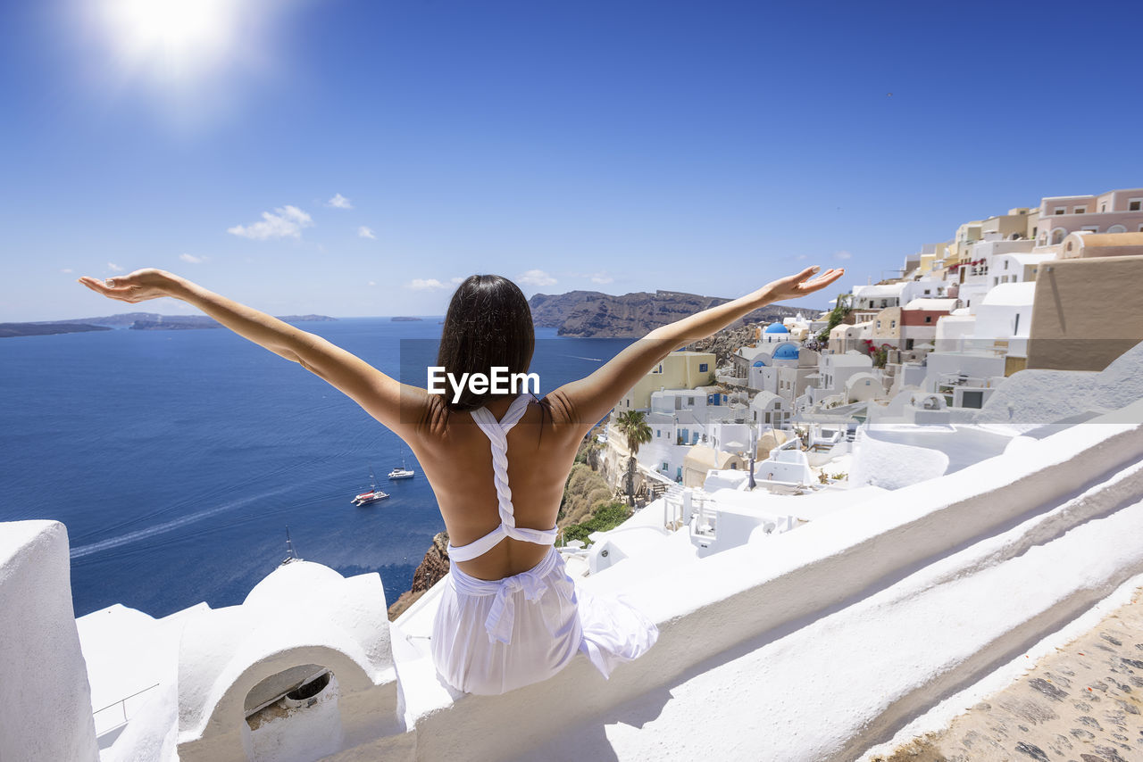 Rear view of woman with arms outstretched sitting against townscape