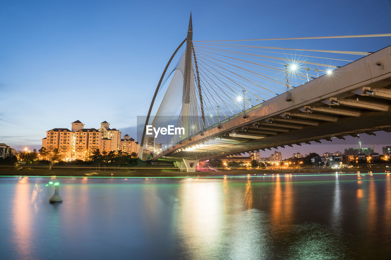 ILLUMINATED BRIDGE OVER RIVER AGAINST SKY IN CITY