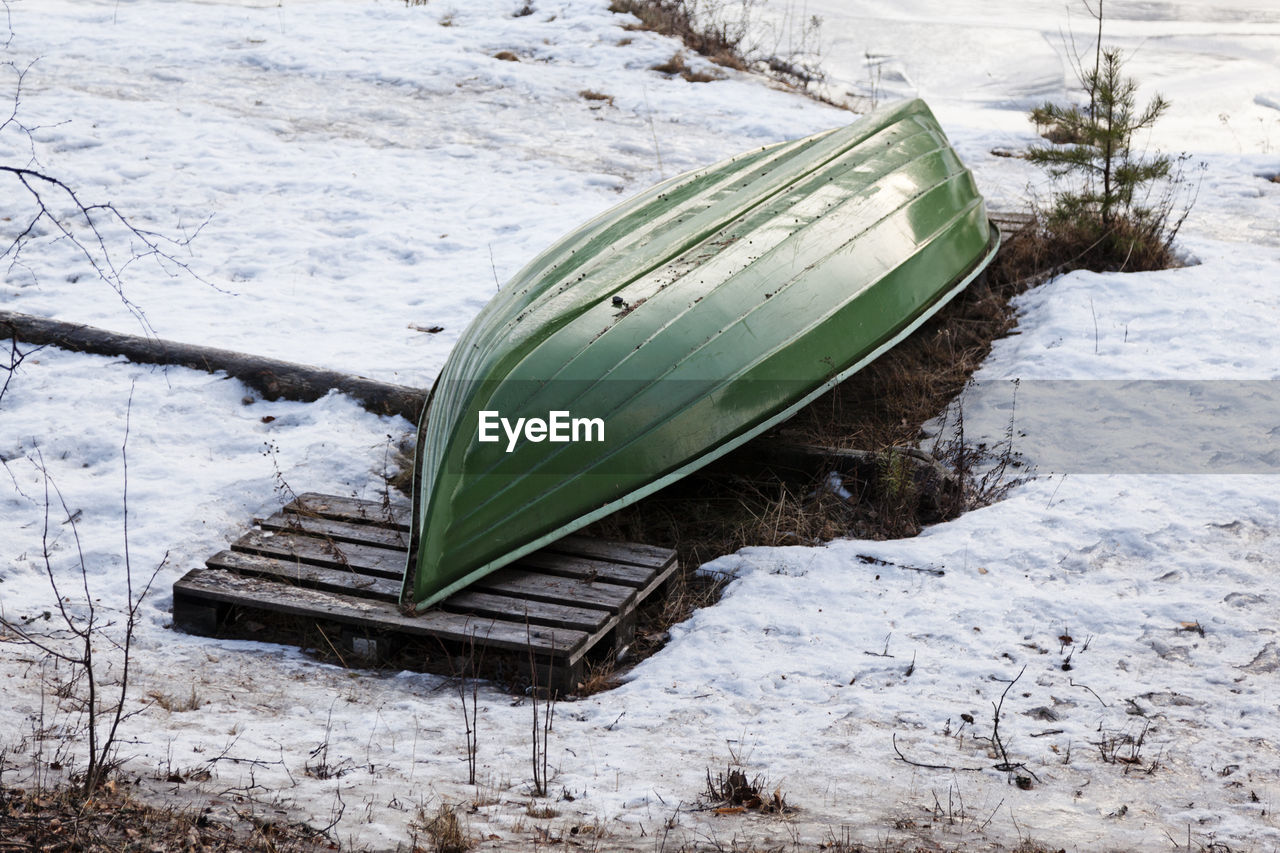 A green boat lying on shore in anticipation of summer