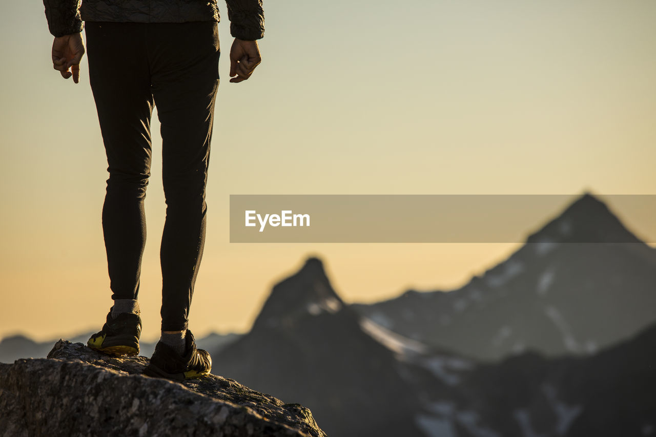 Lower half of trail runner standing on mountain summit with view