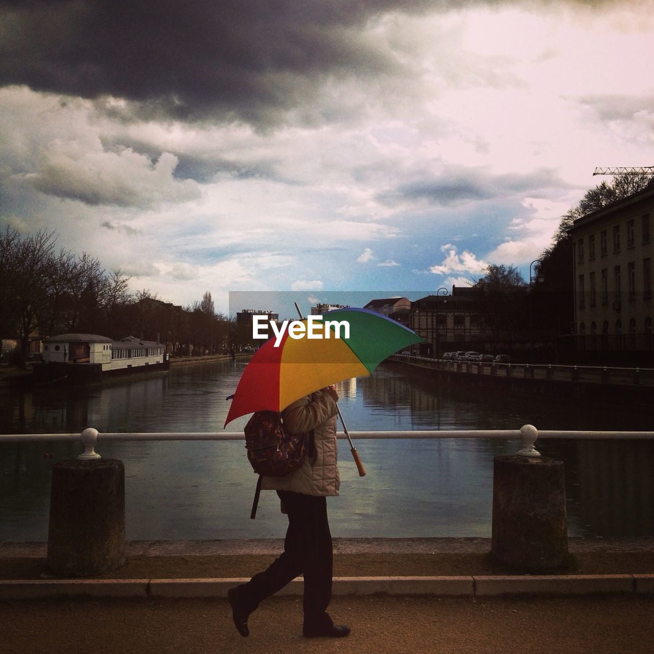 Man with multi colored umbrella walking along bridge