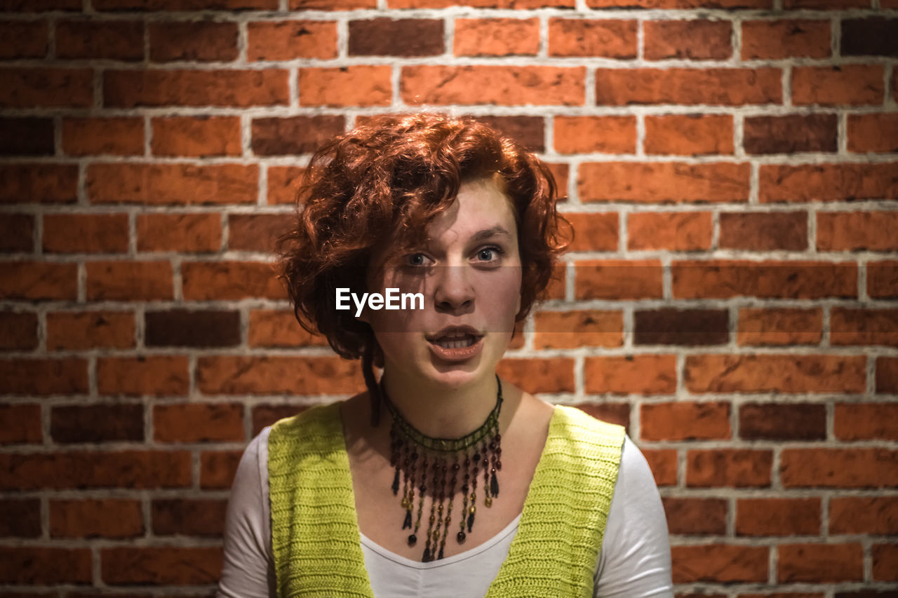 Portrait of young woman against brick wall