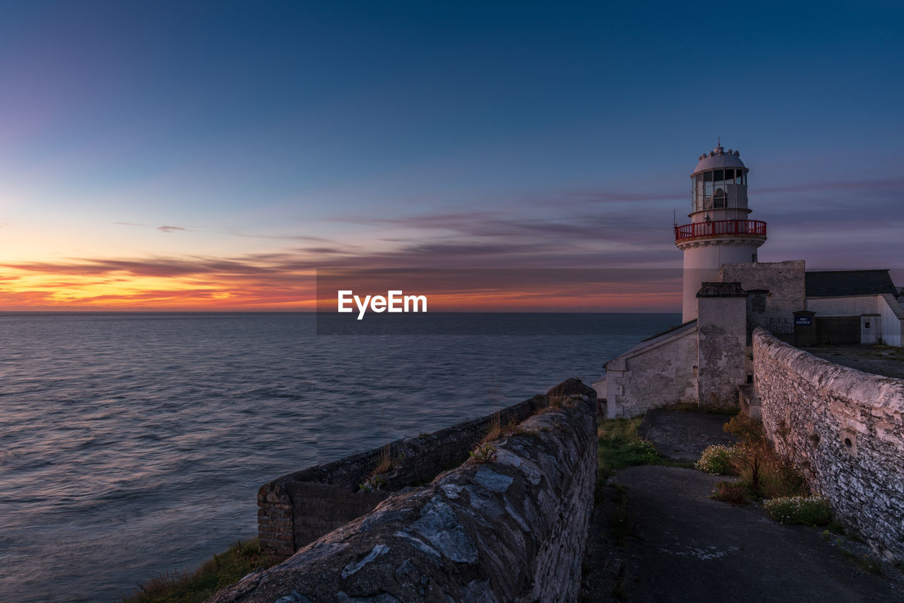 Lighthouse by sea against sky during sunset