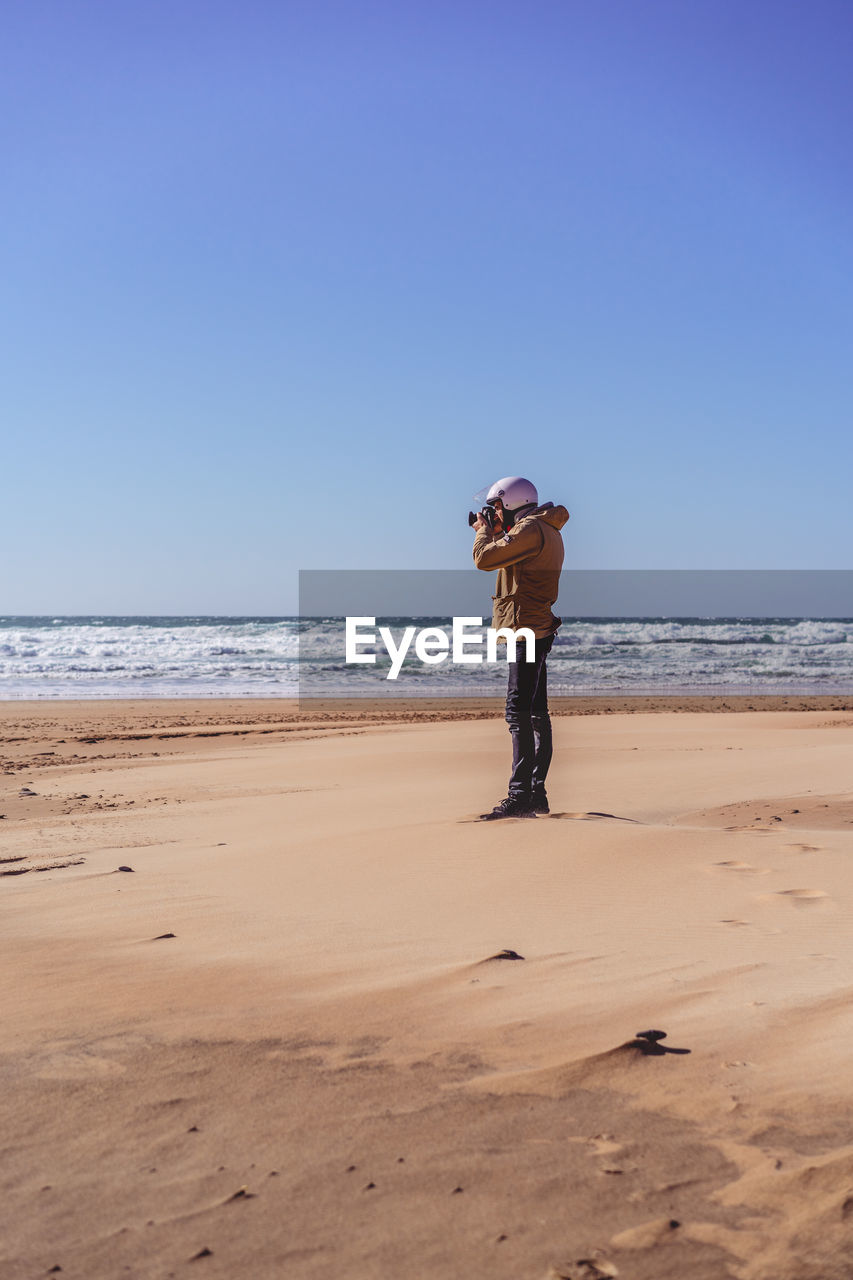 BOY STANDING ON BEACH AGAINST SKY