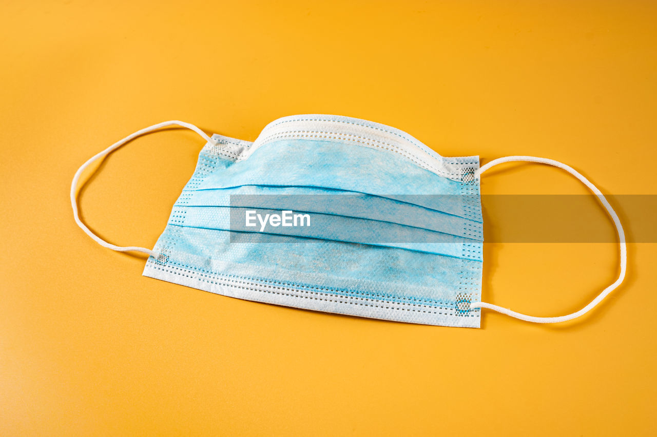 High angle view of surgery mask on table against yellow background