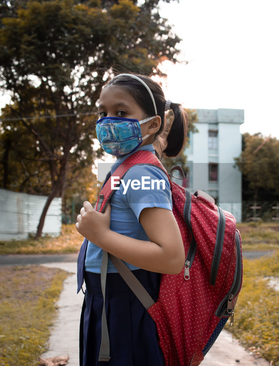 Portrait of a happy indian girl child student in blue school uniform and nose mask going to school