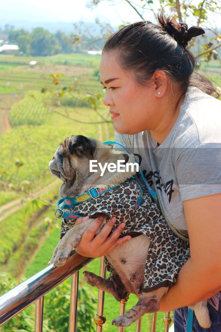 Side view of overweight woman carrying dog while looking at landscape