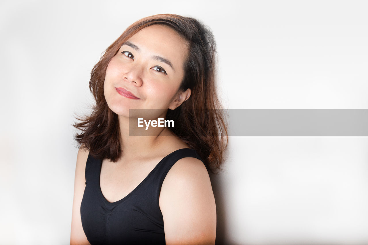 PORTRAIT OF SMILING WOMAN AGAINST WHITE BACKGROUND