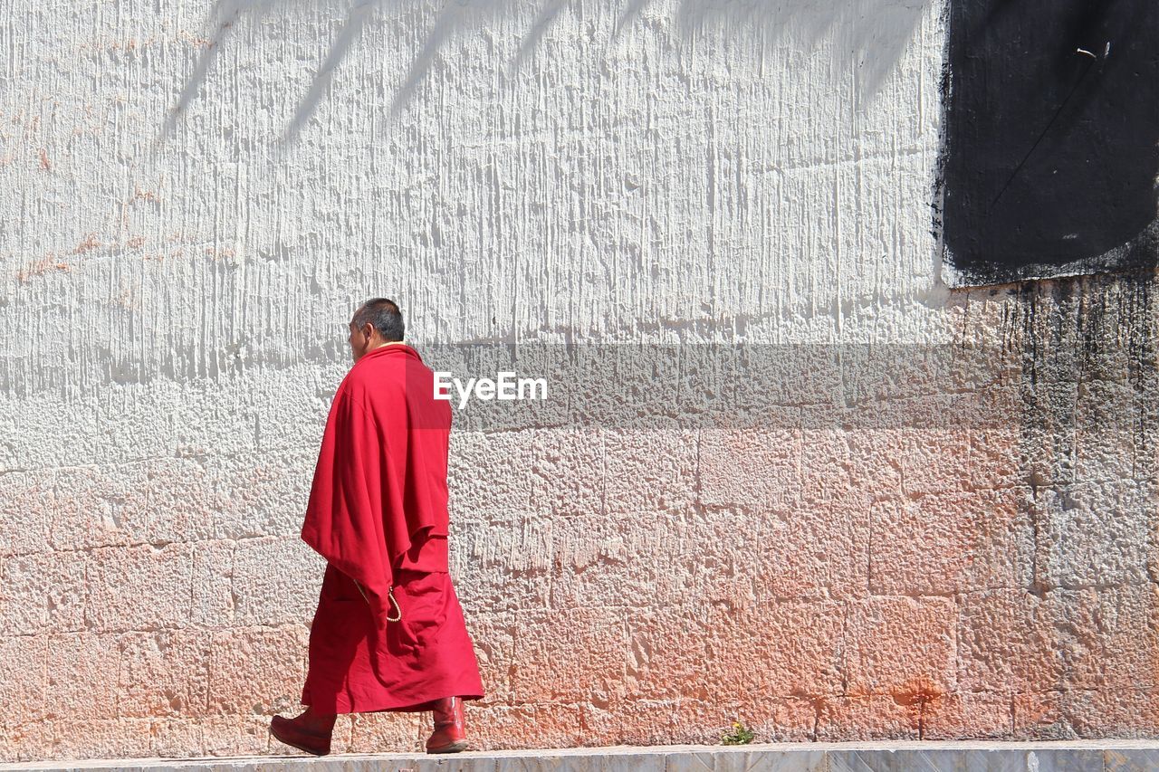 Monk walking on footpath by wall