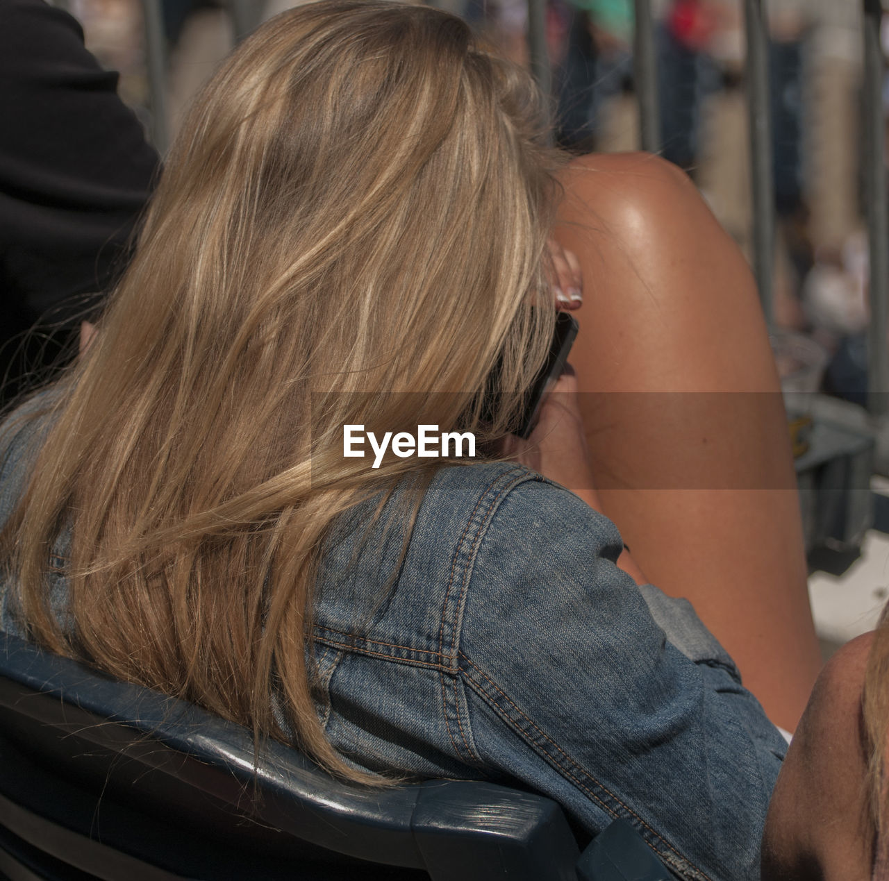Rear view of woman wearing denim jacket sitting on chair