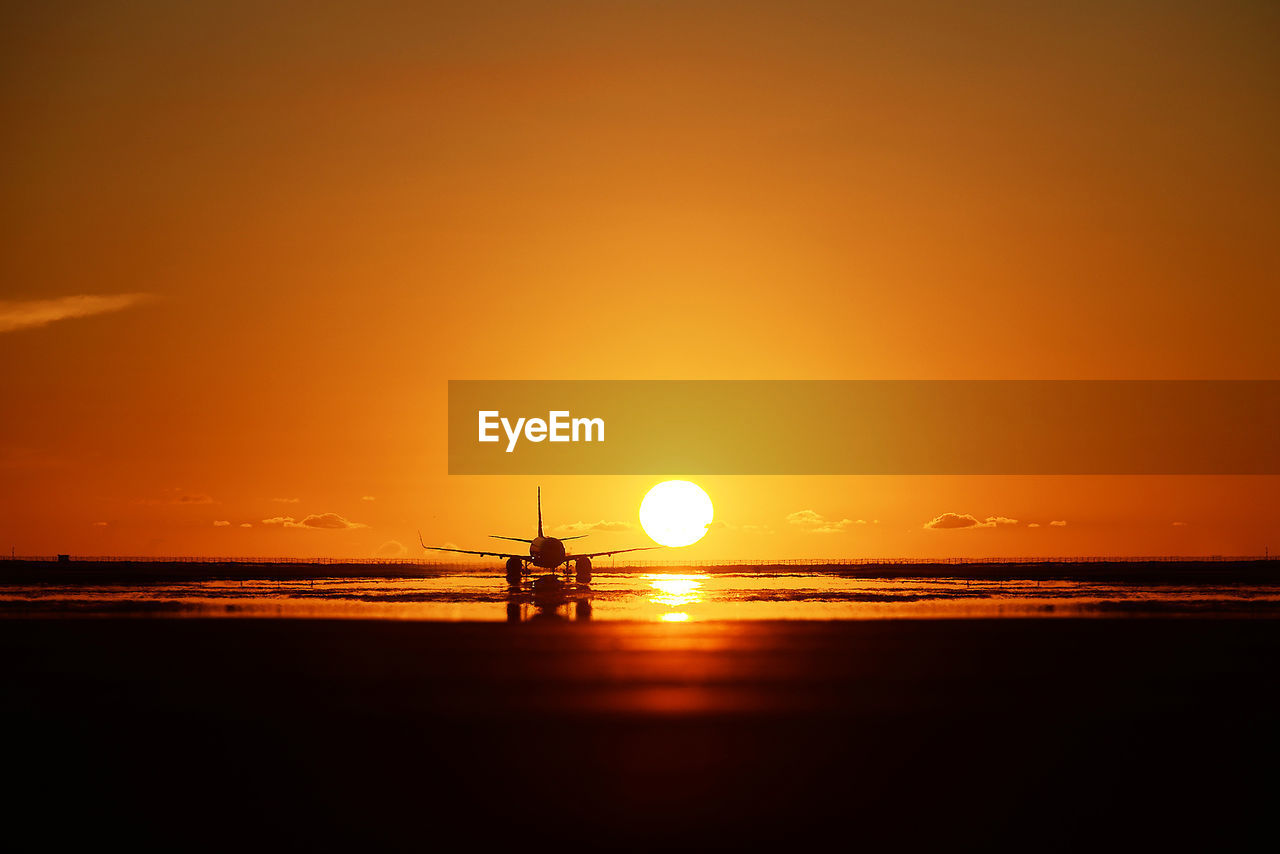 Silhouette airplane on beach against sky during sunset