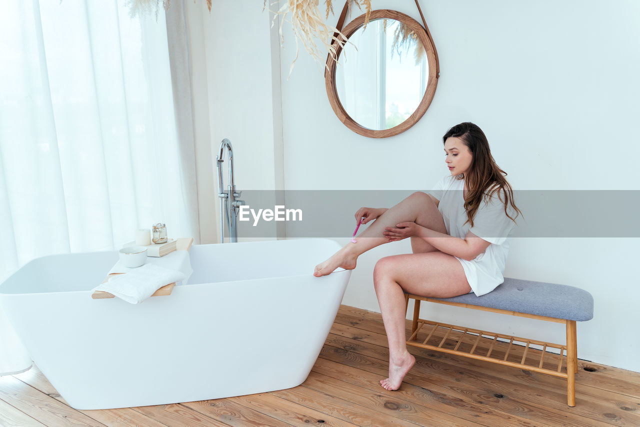 Woman shaving legs while sitting at home