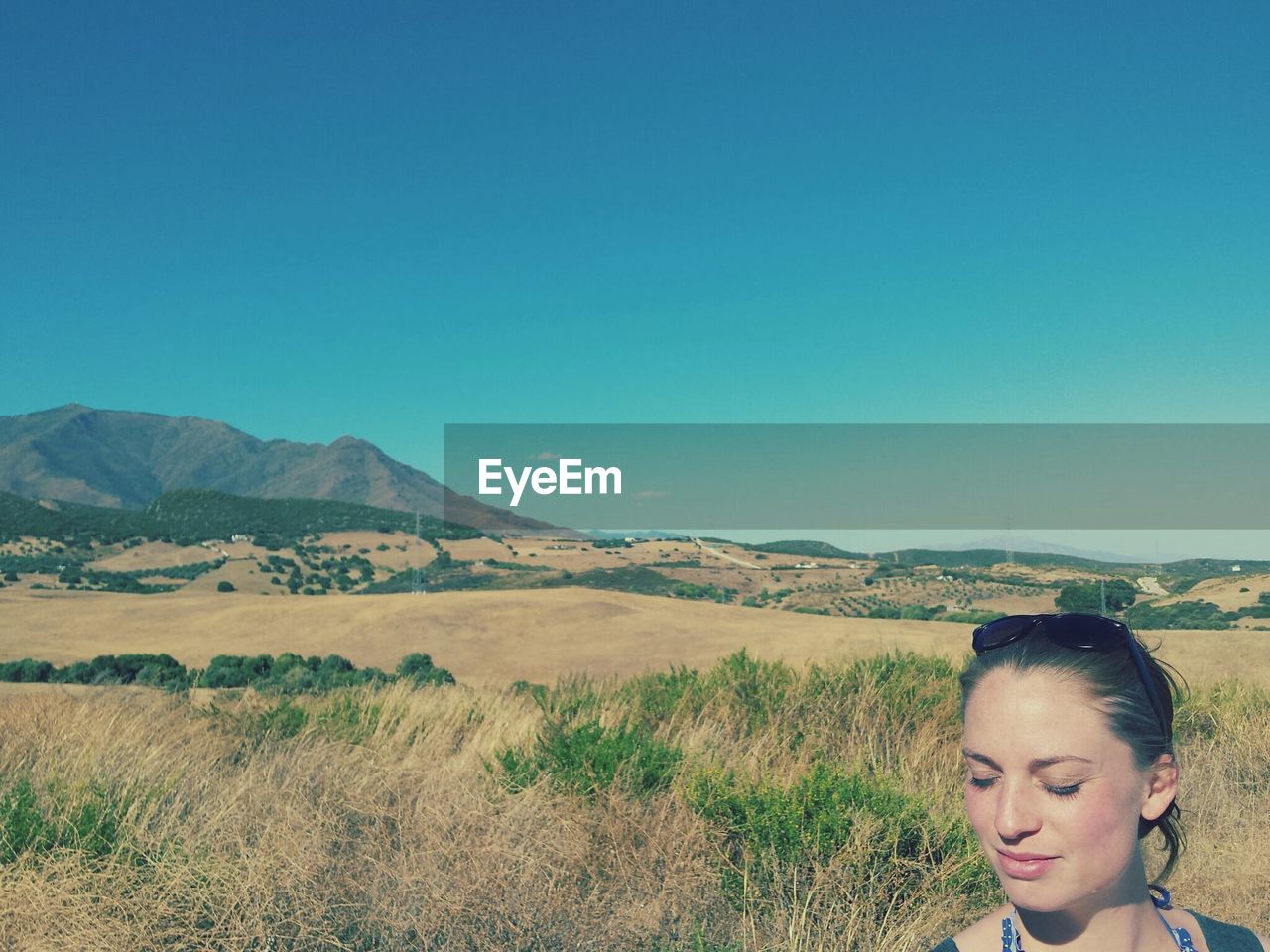 Beautiful woman with eyes closed on grassy field against clear blue sky