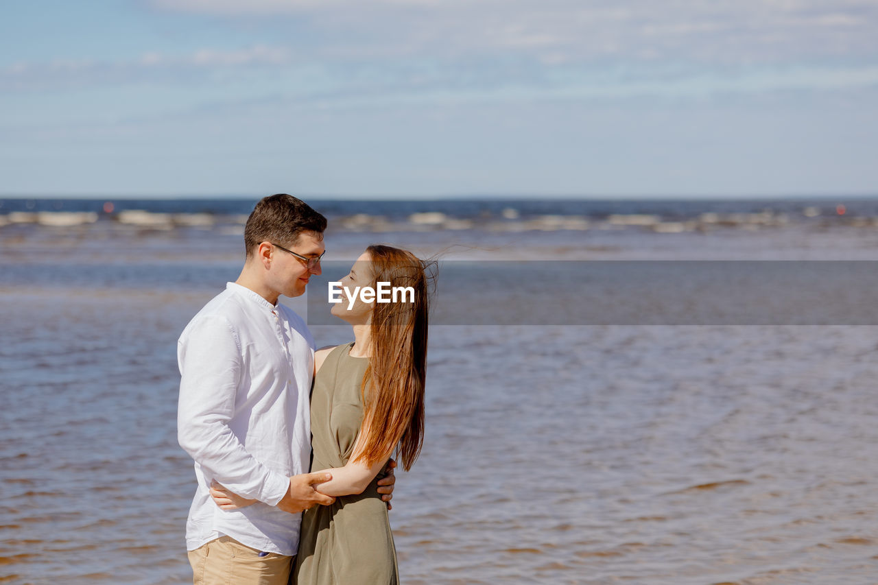 A man and a woman in love embrace portrait of young woman standing at beach