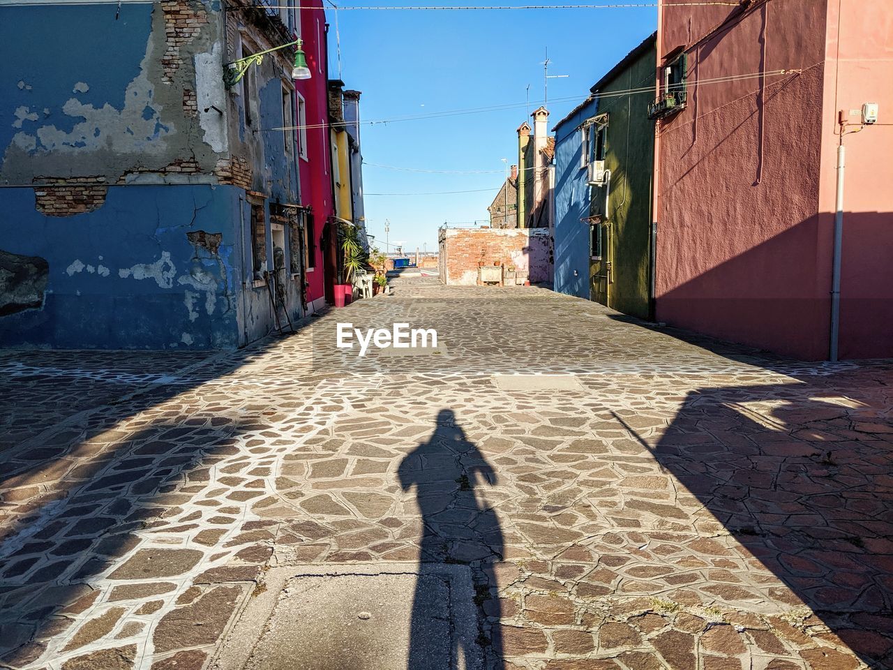 SHADOW OF PERSON ON FOOTPATH AMIDST BUILDINGS