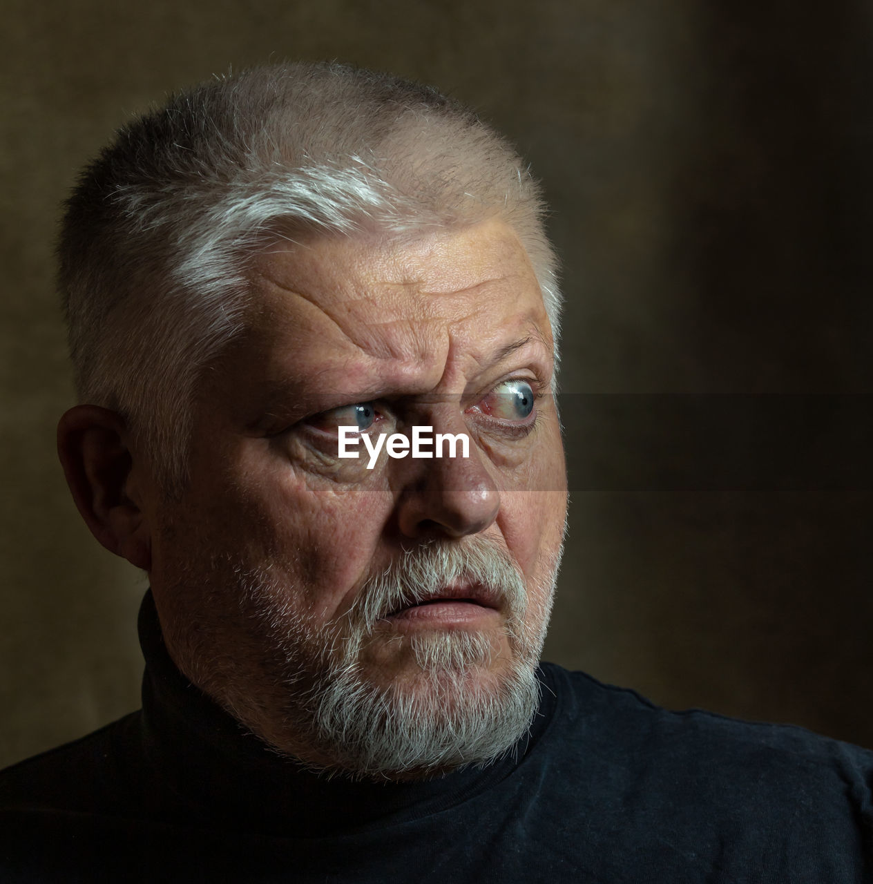 Portrait of an elderly man in classic rembrandt light. the person looks to the side, startled.