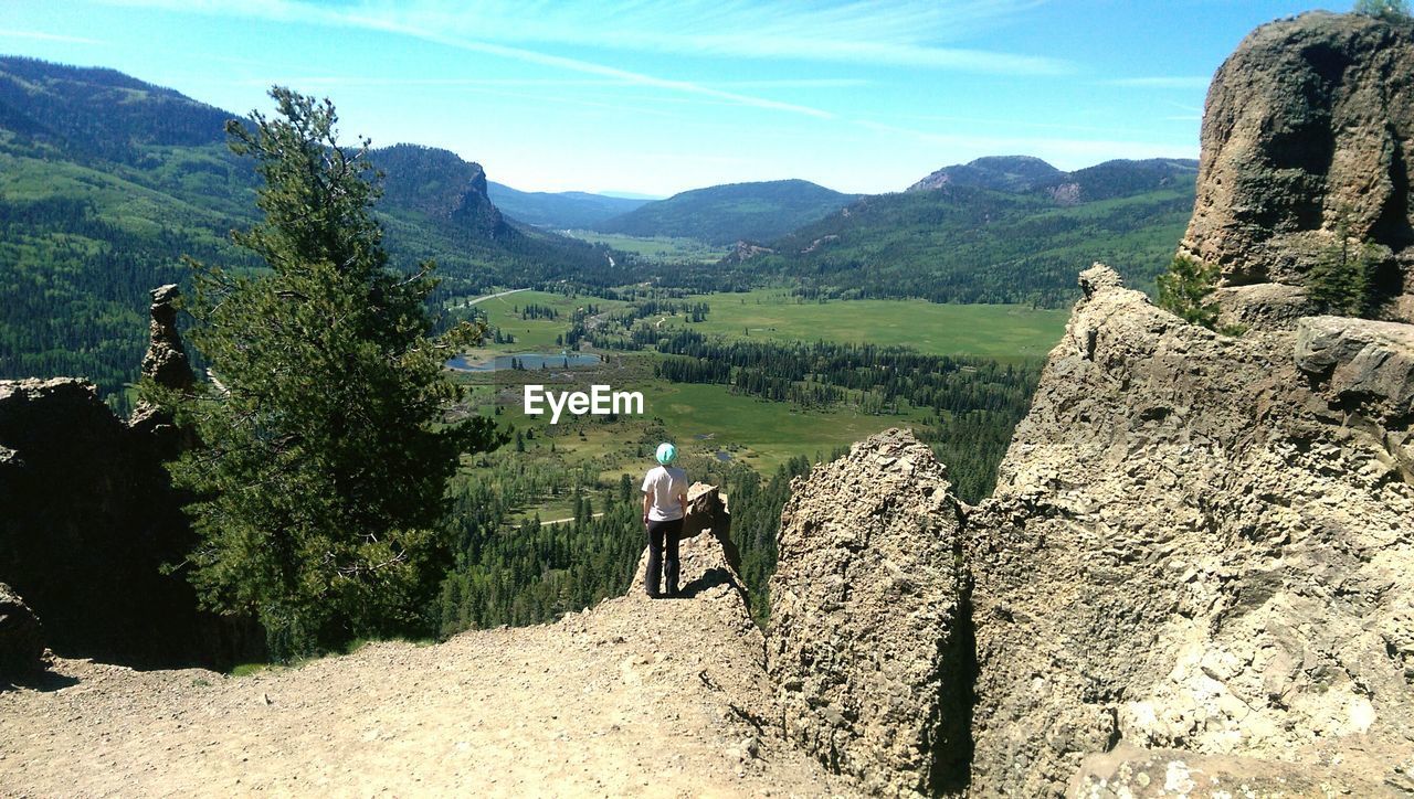 Rear view of woman standing on rocky mountain against sky