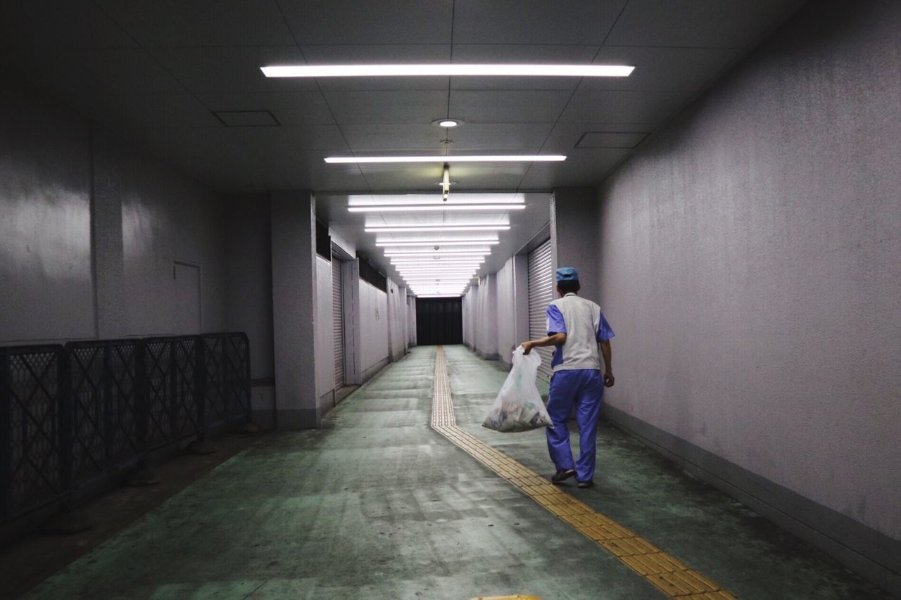 Rear view of man walking in illuminated corridor