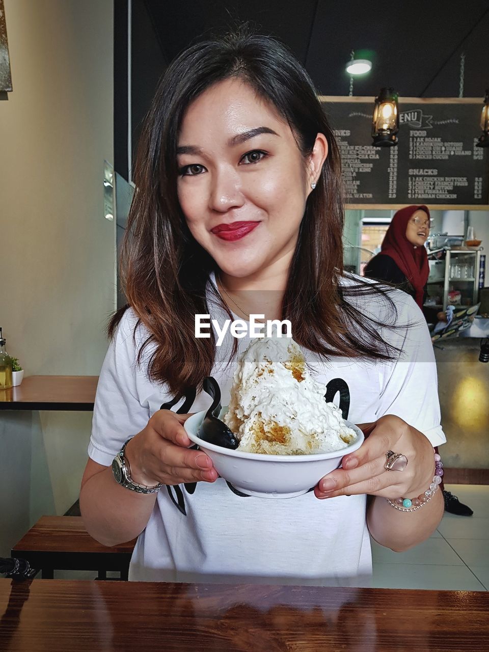 Portrait of smiling woman holding bowl with dessert at cafe